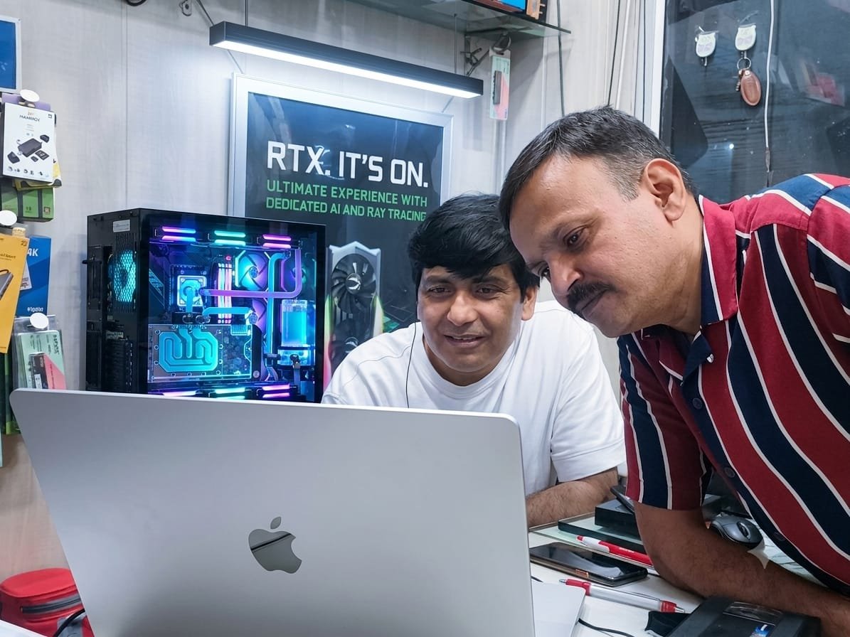 Two of the team at the counter in Husainganj, going through a build on a laptop beside a watercooled RGB tower